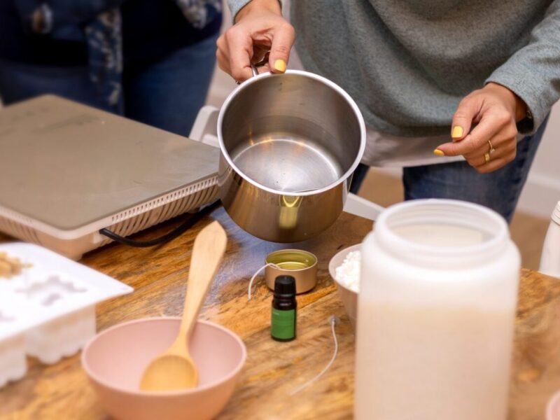 Artisan versant de la cire fondue dans un moule pour fabriquer une bougie artisanale.